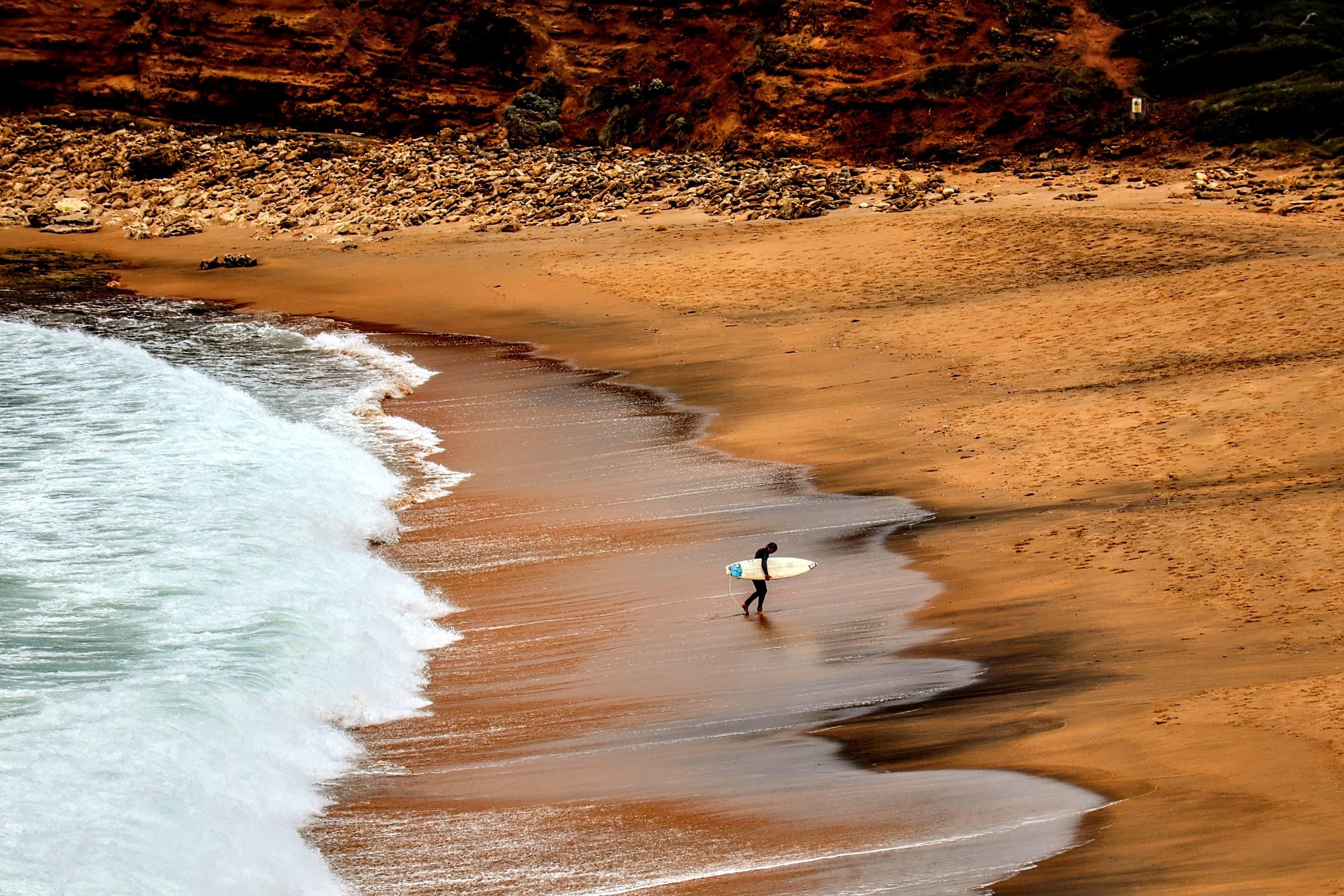 A surfer walking along a beach with a surfboard